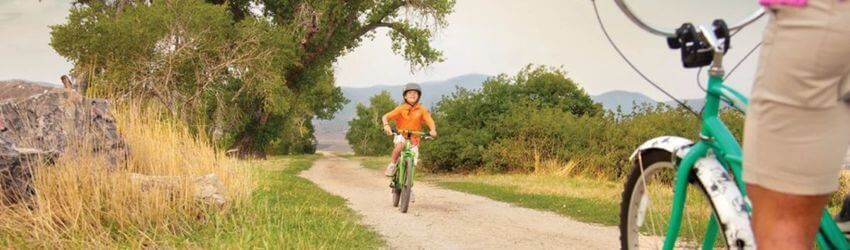 Child biking on rural path with adult nearby.
