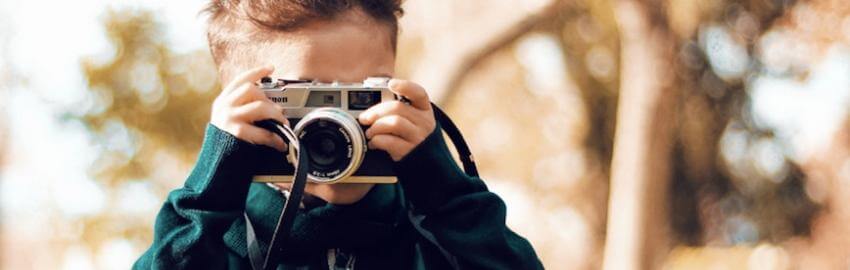 Child photographing with a vintage camera outdoors.