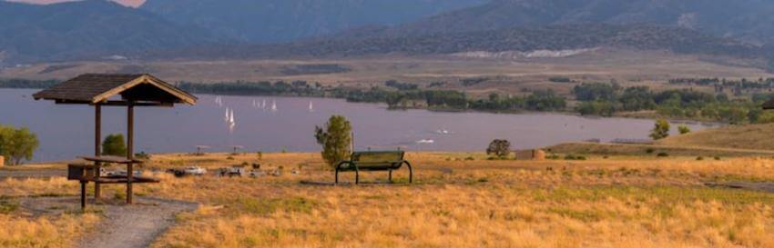 Bench overlooks scenic lake and distant sailboats at sunset.