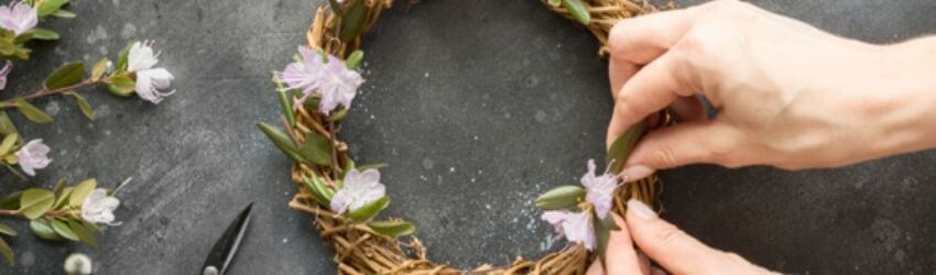 Hands arranging flowers on a woven wreath.