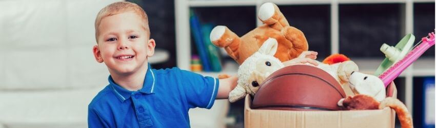 Smiling child with toys in a cardboard box.