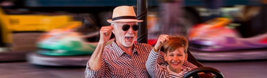 Elderly man and child joyfully riding bumper car.