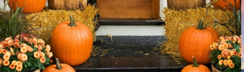 Pumpkins and flowers on porch steps with hay bales.