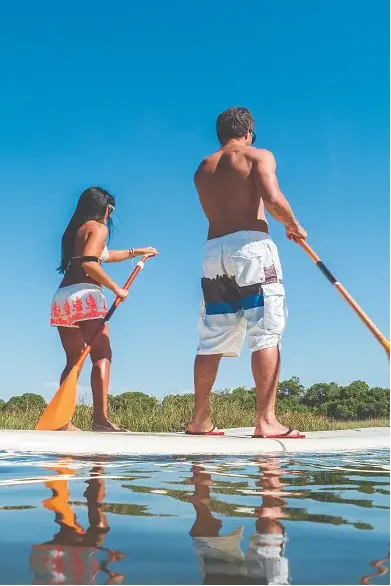 Couple paddleboarding on calm water under blue sky