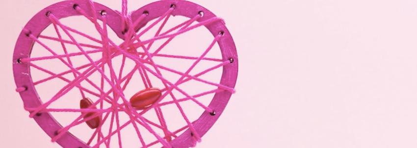 Pink string heart hanging on pink background.