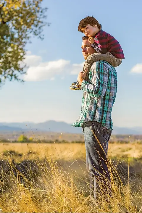 Father carrying child on shoulders in open grassy field
