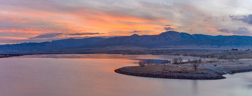 Sunset over tranquil lake and distant mountain range.