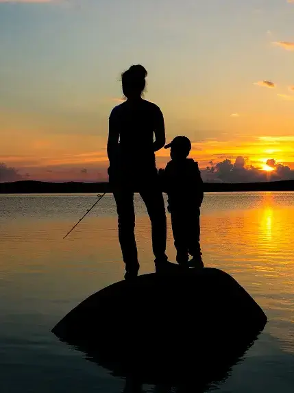 Silhouette of parent and child standing by lake during sunset