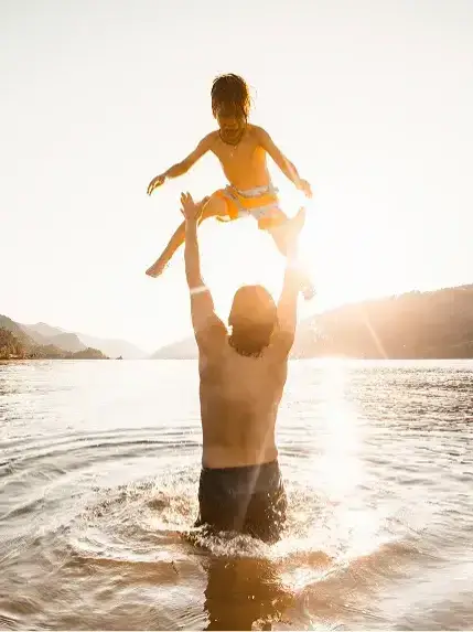 Parent lifting child in lake water during sunset