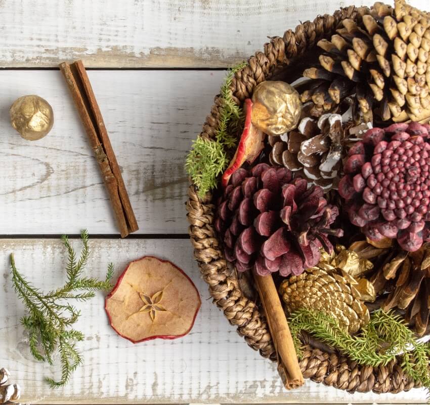 Wicker basket with pinecones and cinnamon on table.