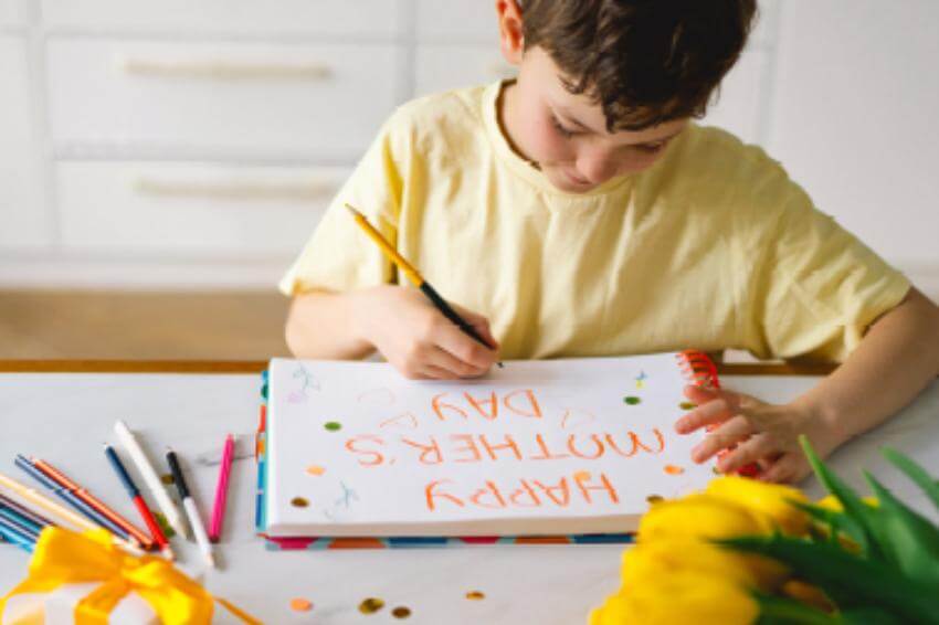 Child drawing a Mother's Day card at table.