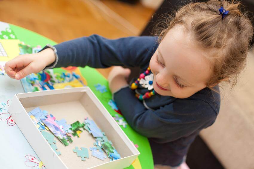Child assembling colorful puzzle pieces on table.