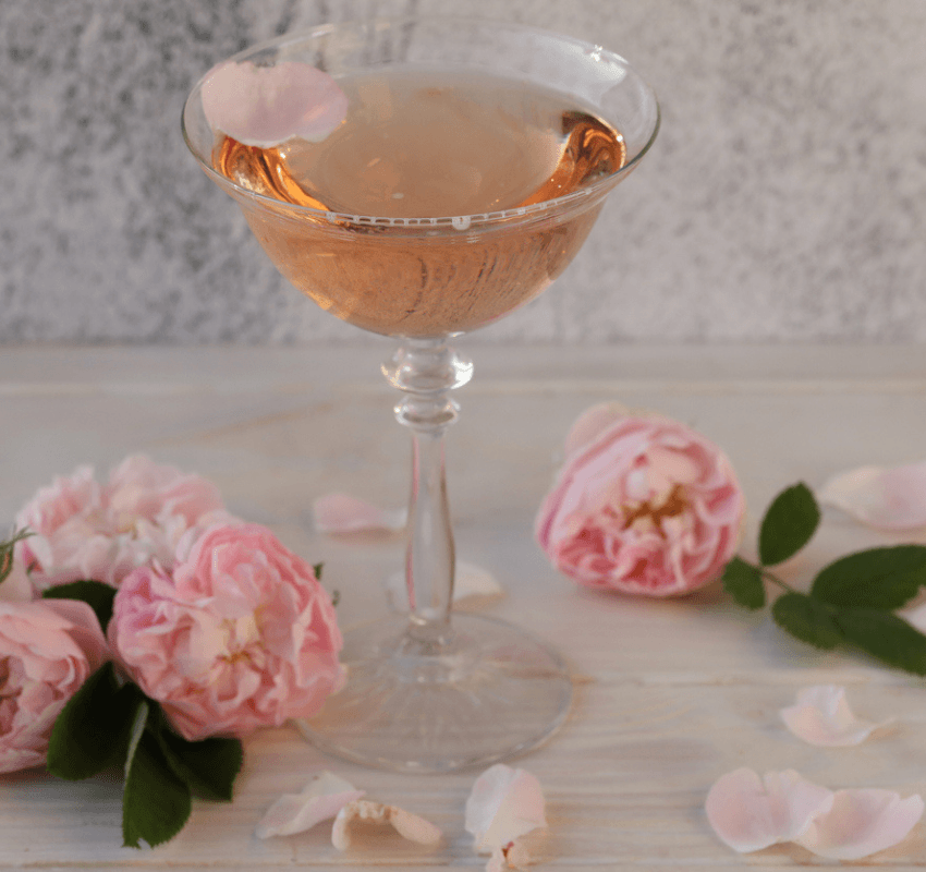 Glass of rosé wine with pink roses nearby.