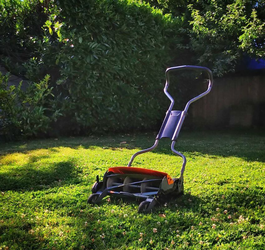 Lawn mower resting on a sunlit, grassy yard.