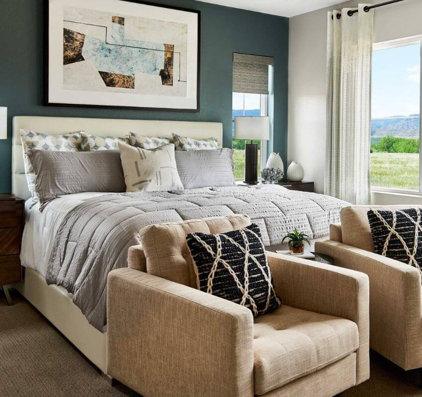 Cozy bedroom with bed, armchairs, and large window view.