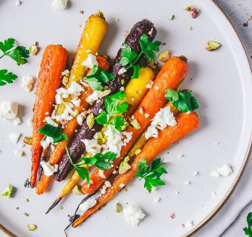 Roasted carrots garnished with cheese and fresh herbs.