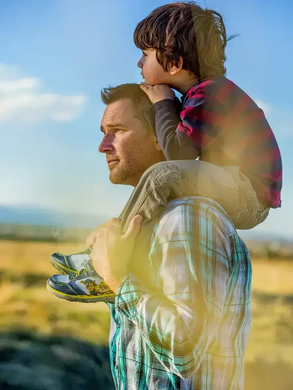 Father carrying his son outdoors while enjoying scenic open space near the Solstice community