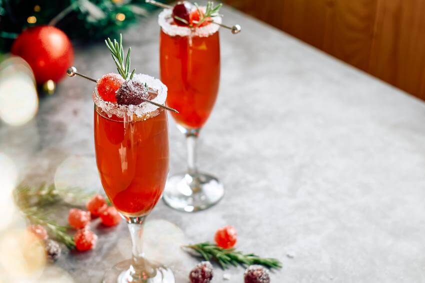 Two festive cocktails with sugared cranberries and rosemary.
