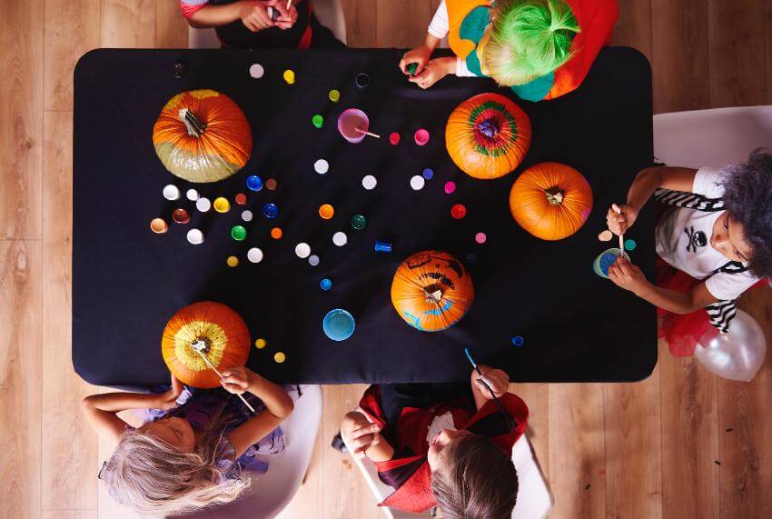 Children painting pumpkins at a table.