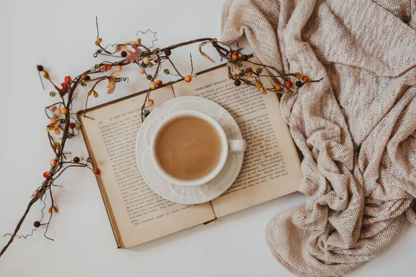 Open book with coffee and cozy blanket nearby.
