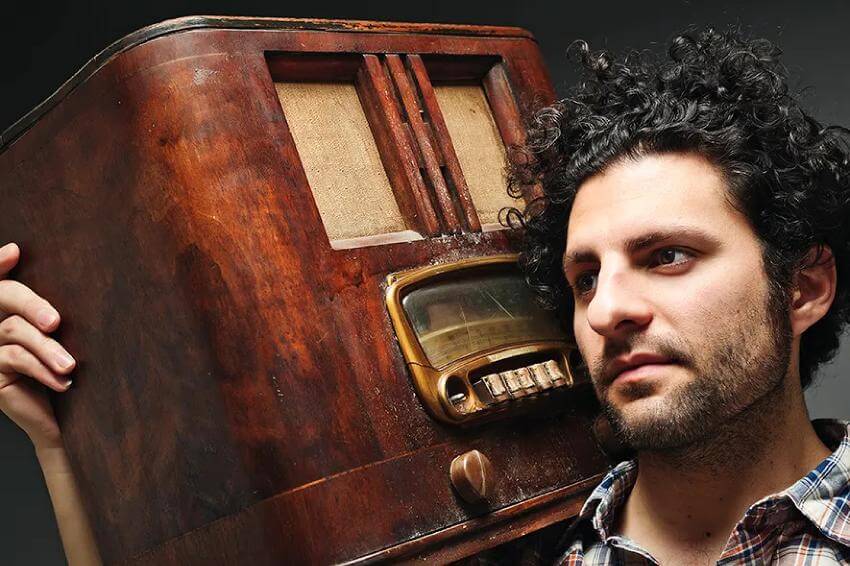 Man holding vintage wooden radio, looking contemplative.