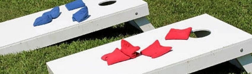 Cornhole boards on grass with red and blue bags.